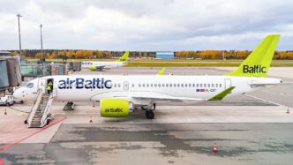 Airbus A220-300 v zelenobílých barvách airBaltic stojí u nástupních schůdků na odbavovací ploše.