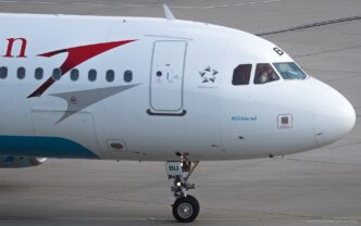 Airbus A320 s červeným šípem a nápisem Austrian na bílém trupu stojí na letištní ploše.