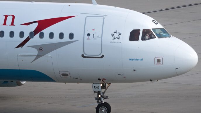 Airbus A320 s červeným šípem a nápisem Austrian na bílém trupu stojí na letištní ploše.