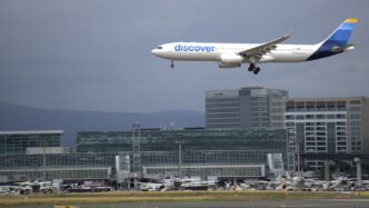 Airbus A330 s nápisem discover na trupu klesá k přistání nad budovou letištního terminálu.