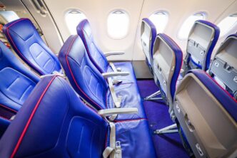 Interiér kabiny Airbusu A321neo s fialovými sedadly a otevřenými schránkami na příruční zavazadla nad hlavou.