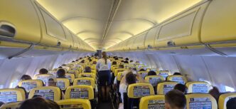 Pohled uličkou kabiny Boeingu 737 se žlutomodrými sedadly a schránkami na příruční zavazadla nad hlavou.