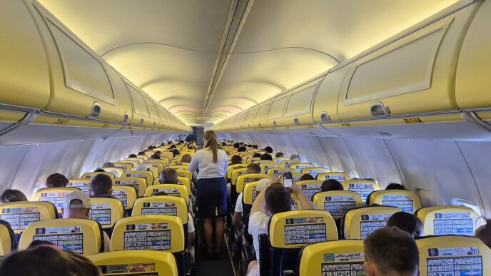 Pohled uličkou kabiny Boeingu 737 se žlutomodrými sedadly a schránkami na příruční zavazadla nad hlavou.
