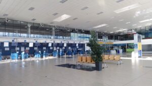 Odbavovací hala regionálního letiště s řadou uzavřených přepážek check-in, sedačkami a prosklenou stěnou