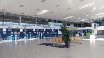 Odbavovací hala regionálního letiště s řadou uzavřených přepážek check-in, sedačkami a prosklenou stěnou