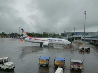 Boeing 737 MAX 8 v modro-oranžových barvách Smartwings stojí na mokré odbavovací ploše, v popředí zavazadlové vozíky.
