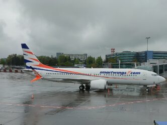 Boeing 737 MAX 8 v barvách Smartwings stojí na stojánce před budovou terminálu, na trupu je nápis smartwings.com.